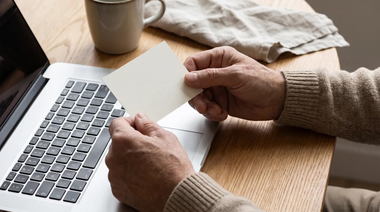 Hands holding a payment card at a laptop during an online financial services transaction